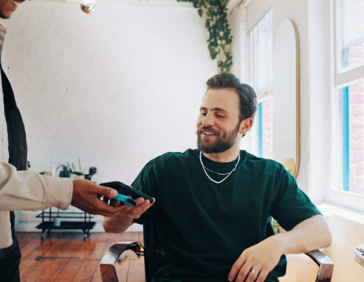 Happy man, hairdresser or customer with phone for payment, banking app or pos machine in salon. Male people, barber or client with mobile smartphone for tap to pay or wireless transaction in parlor.