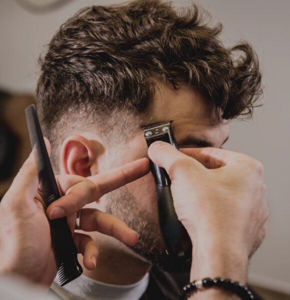 Young man with trendy haircut at barber shop. Barber does the hairstyle and beard trim. Concept barbershop.